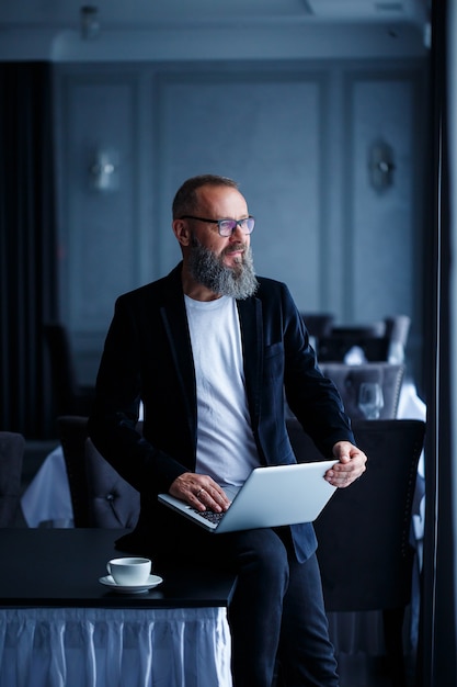 Een volwassen zakenman met een baard in een bril zit met een laptop op zijn schoot en werkt. De manager stelt een workflowschema op