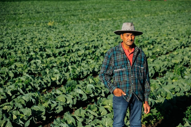 Een vooraanzicht van een boer zittend in een groenteveld met zijn armen gekruist