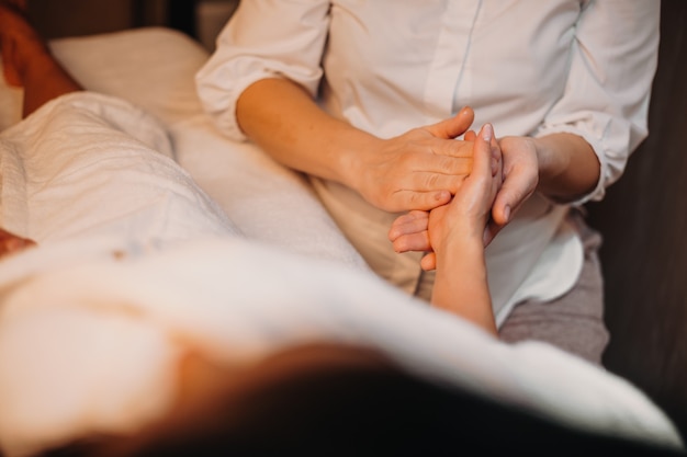 Een voorzichtige blanke masseur masseert de hand van de cliënt terwijl ze op de bank ligt tijdens een spa-procedure