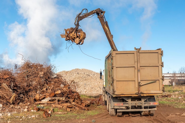 Foto een vrachtwagen met een kraan laadt een stapel schroot in een afvalcontainer