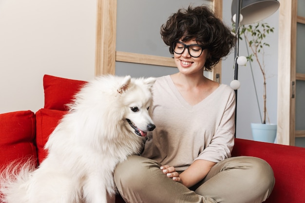 een vrij gekrulde vrouw zittend op de bank met haar schattige witte hond.