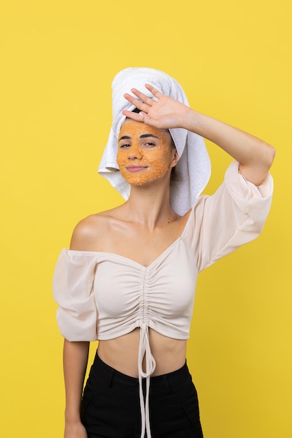 Een vrij jong meisje met een scrubmasker op haar gezicht poseert voor de camera en glimlacht tegen een gele achtergrond