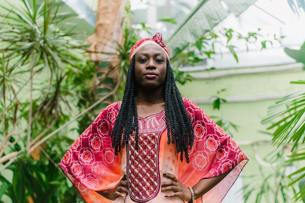 Foto een vrij jonge afro-amerikaanse vrouw staat onder palmbomen in de jungle en glimlacht breed in een nationaal afrikaans kostuum.