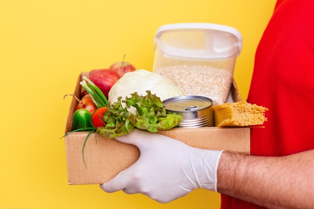 Een vrijwilliger brengt een doos met verse groenten en boodschappen in een kartonnen doos op een gele backg