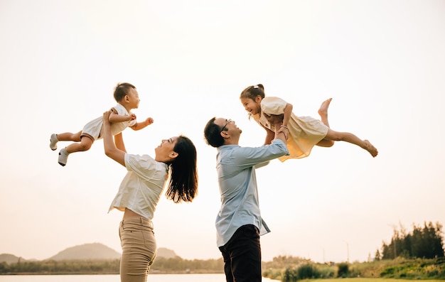 Een vrolijk Aziatisch gezin geniet van een dagje uit in de natuur, terwijl vader en moeder hun peuter in de zonnige lucht gooien. Het blije kind geniet van de speelse vrijheid van het vliegen, vastgelegd op een foto