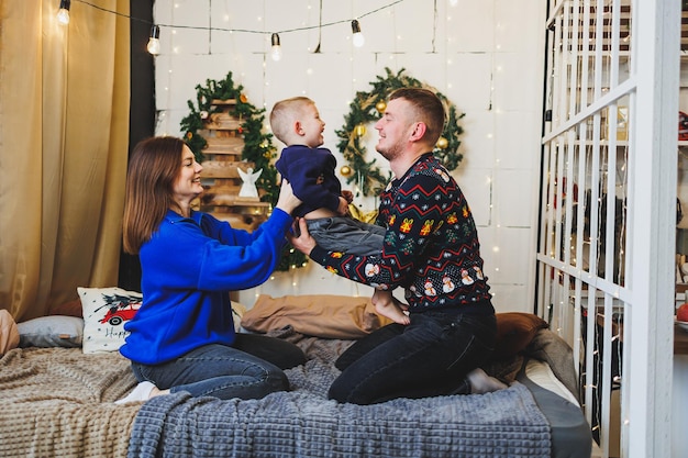 Foto een vrolijk jong gezin met een klein kind rust thuis bij de kerstboom familiepaar met kerstversiering thuis kerstmis nieuwjaar tijd om te vieren