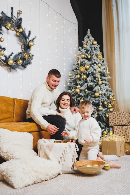 Een vrolijk jong gezin met een klein kind rust thuis bij de kerstboom Familiepaar met kerstversiering thuis Kerstmis Nieuwjaar tijd om te vieren