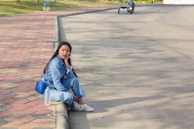 Een vrolijk jong meisje dat in het park in de stad zit, houdt een mobiele telefoon vast met een waterfles op het levensstijlconcept aan de zijkant