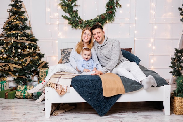 Een vrolijk jong stel met een zoontje speelt op het bed bij de kerstboom Nieuwjaarsinterieur in de slaapkamer Kerstboom met speelgoed Feestelijke familiesfeer