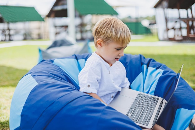 Een vrolijk kind speelt op kleurrijke zitzakken op straat Een kleine jongen kijkt tekenfilms op een laptop terwijl hij op een stoel in het park zit