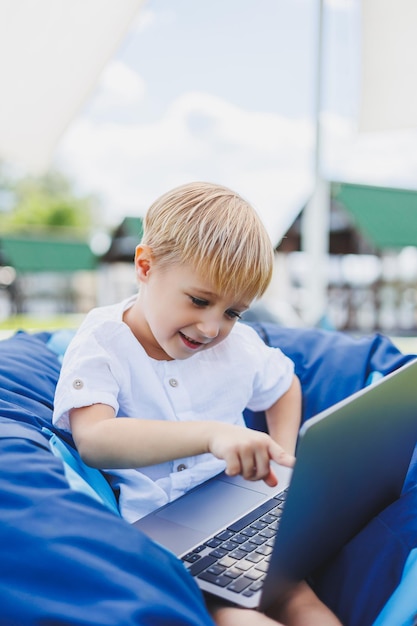 Een vrolijk kind speelt op kleurrijke zitzakken op straat Een kleine jongen kijkt tekenfilms op een laptop terwijl hij op een stoel in het park zit