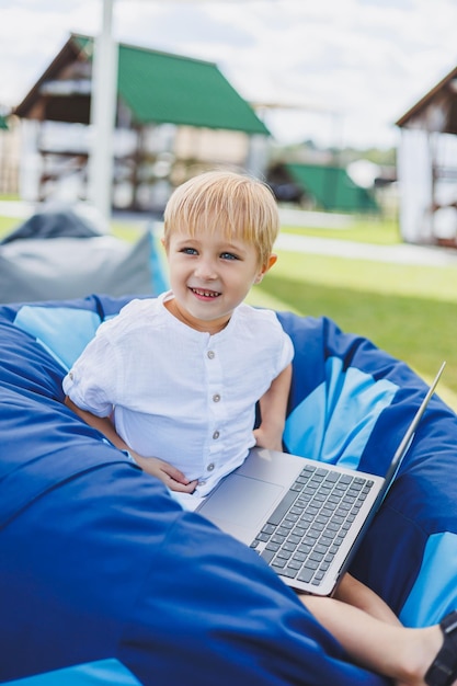 Een vrolijk kind speelt op kleurrijke zitzakken op straat Een kleine jongen kijkt tekenfilms op een laptop terwijl hij op een stoel in het park zit