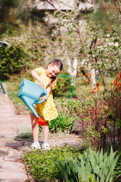 Een vrolijk lachend meisje in een gele jurk geeft jonge scheuten planten water in de achtertuin op een wa...