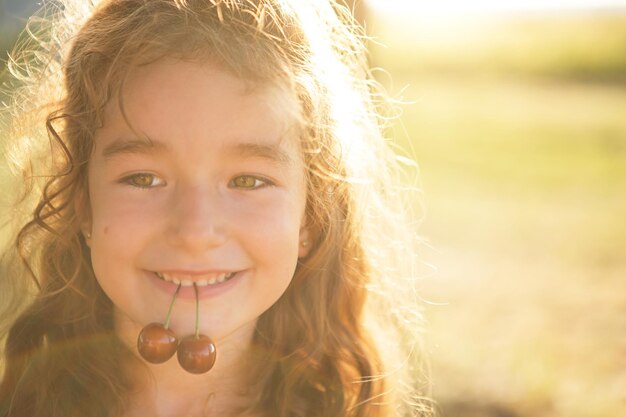 Een vrolijk lief meisje met kersenbessen in haar mond Grappig zomerportret van een kind met een kerscadeaus van zomerzomertijd