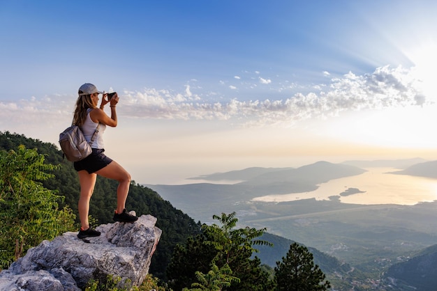 Een vrolijk meisje met een rugzak fotografeert de zeegezichten van montenegro vanaf de top van de berg