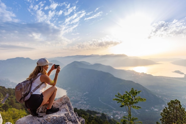 Een vrolijk meisje met een rugzak fotografeert de zeegezichten van montenegro vanaf de top van de berg