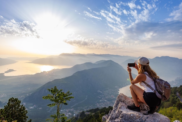 Een vrolijk meisje met een rugzak fotografeert de zeegezichten van montenegro vanaf de top van de berg