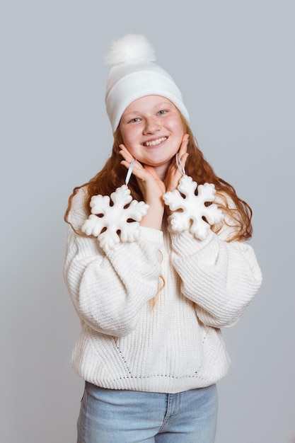 Een vrolijk meisje met rood haar in een witte trui en hoed houdt sno . vast