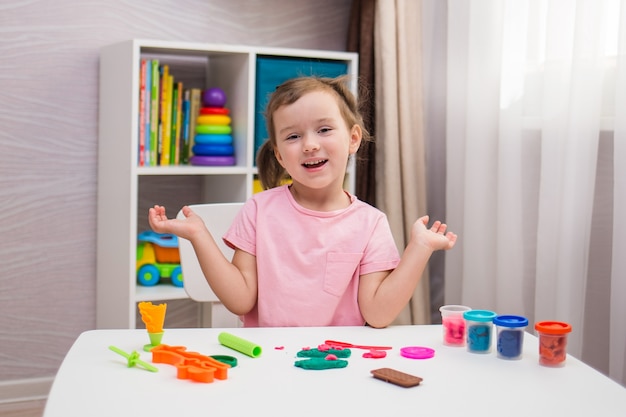 Een vrolijk meisje speelt play-doh aan een tafel in de kinderkamer