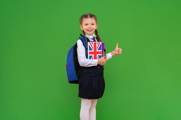 Een vrolijk schoolmeisje met een Engels leerboek. een meisje in een schooluniform. kennis opdoen door vreemde talen te leren. geïsoleerde achtergrond.