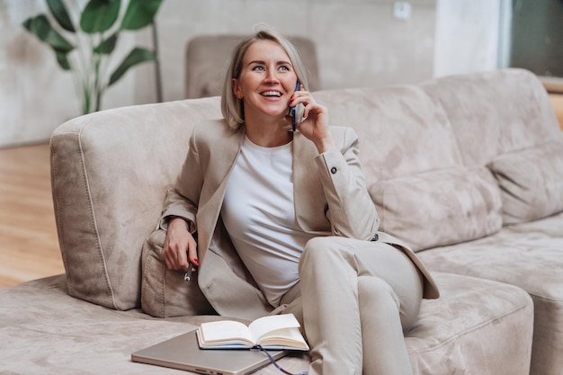 Een vrolijke Amerikaanse zakenvrouw die telefonisch praat, zit op een knusse bank op kantoor met een brede glimlach, geweldig nieuws