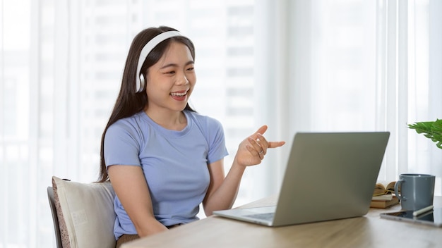 Een vrolijke Aziatische vrouw met een koptelefoon praat tijdens een online vergadering of online sollicitatiegesprek