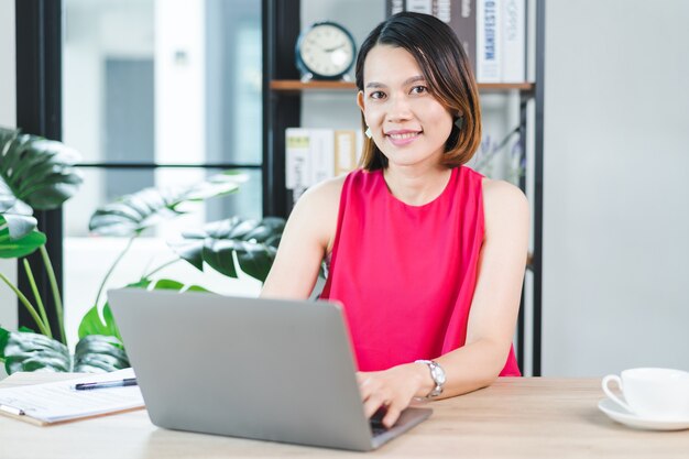 Een vrolijke Aziatische zakenvrouw van middelbare leeftijd in ontspannen vrijetijdskleding die thuis werkt, e-mail controleert op computerlaptop, schrijft op documentpapier voor financiële boekhouding. Zakelijke stockfoto