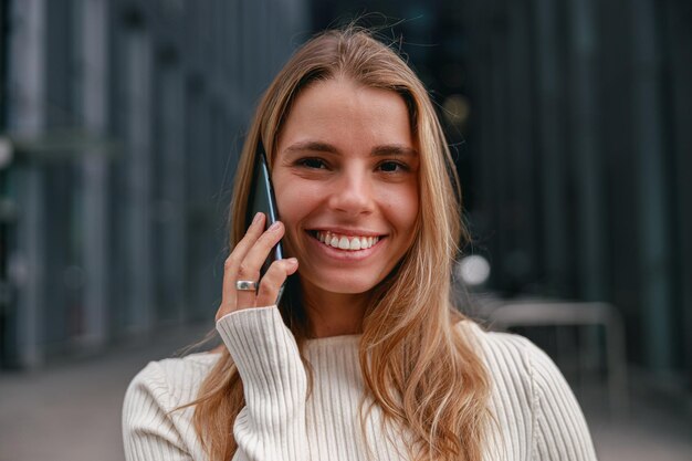 Een vrolijke en aantrekkelijke jonge vrouw die gelukkig een telefoon vasthoudt in een levendige stedelijke omgeving