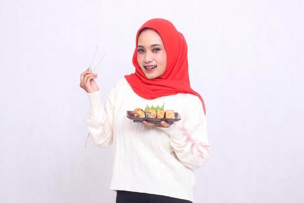 Een vrolijke Indonesische vrouw met een hijab op de camera pakt met eetstokjes op en brengt op een