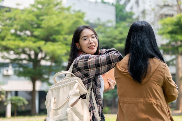 Een vrolijke jonge aziatische vrouw glimlacht naar de camera terwijl ze met haar vriendin in het campuspark loopt.