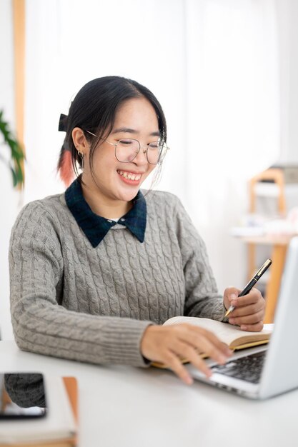 Een vrolijke jonge Aziatische vrouwelijke universiteitsstudent studeert online in een café coworking space