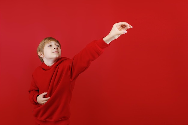Een vrolijke jongen in een rood pak strekt zijn hand naar voren en probeert iets te grijpen