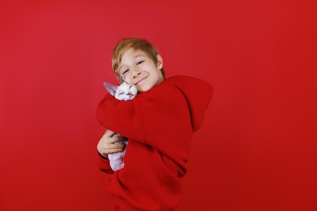 Een vrolijke jongen in een rood trainingspak knuffelt een klein katje en knuffelt hem