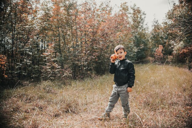 Een vrolijke jongen in het herfstbos met een appel in zijn handen