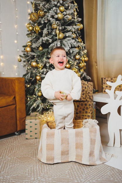 Een vrolijke kleine jongen van 23 jaar oud staat bij een kerstboom omringd door slingers en Kerstmis presenteert het concept van een kerstverhaal, een vakantie voor jonge kinderen Kerstboom