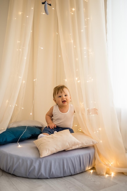 Een vrolijke kleine jongen zit op een matras onder een baldakijn en speelt een blanke babyjongen die in de kinderkamer zit