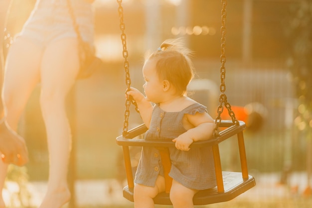 Een vrolijke peuter babymeisje in een jurk op een schommel op de warme zomeravond