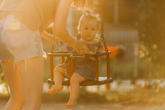 Foto een vrolijke peuter babymeisje in een jurk op een schommel op de warme zomeravond