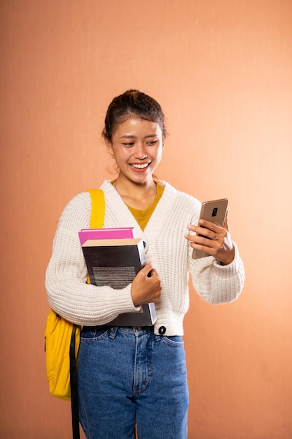 Een vrolijke student is diep betrokken met zowel een smartphone als boeken in de hand