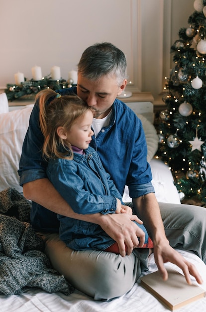 Een vrolijke vader kust een schattig dochtertje bij de kerstboom