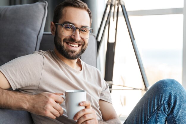 een vrolijke vrolijke jongeman die thuis koffie drinkt.