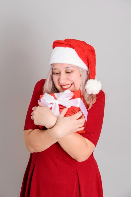 Een vrolijke vrouw in een kerstmuts knuffelt een rode geschenkdoos, verticale foto