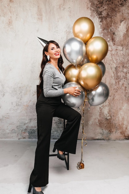 Een vrolijke vrouw met ballonnen lacht een jonge brunette met lang haar viert haar verjaardag heliumballonnen