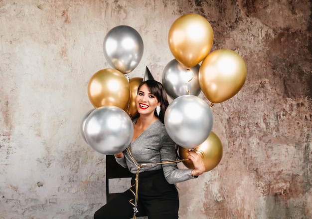 Een vrolijke vrouw met ballonnen lacht een jonge brunette met lang haar viert haar verjaardag heliumballonnen