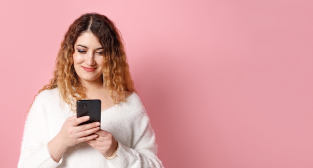 Een vrolijke vrouw staande geïsoleerd op een roze achtergrond met een smartphone