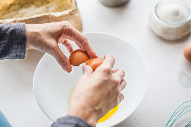 Een vrouw bereidt het deeg voor op de taart, breekt een ei in een kopje. ingrediënten voor het maken van deeg.