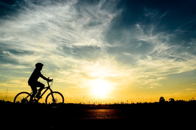 Een vrouw berijdt een fiets op de weg bij zonsonderganghemelachtergrond.