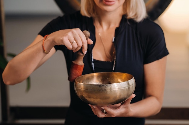 Een vrouw bespeelt een Tibetaanse klankschaal terwijl ze op een yogamat zit tegen de achtergrond van een gong