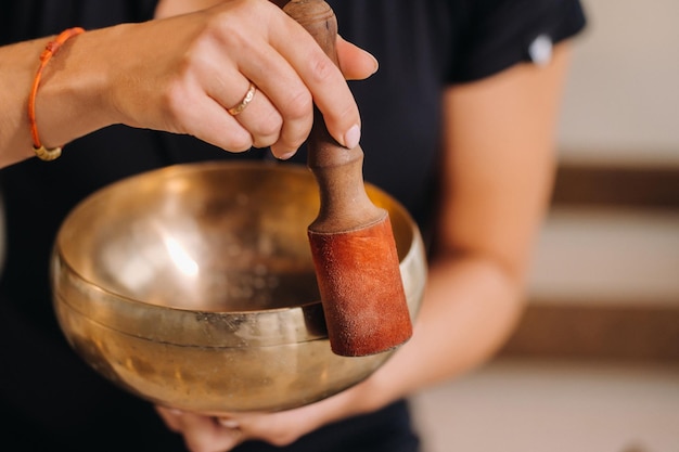 Een vrouw bespeelt een tibetaanse klankschaal terwijl ze op een yogamat zit tegen de achtergrond van een gong