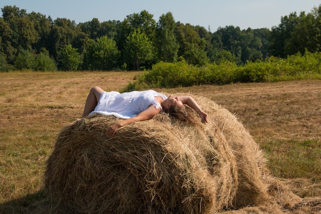 Een vrouw bij een hooiberg in een witte jurk Ochtendzonsopgang in de natuur in het veld